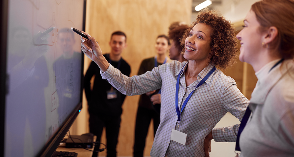 people-at-large-screen stock photo of woman pointing to large screen as several people watch