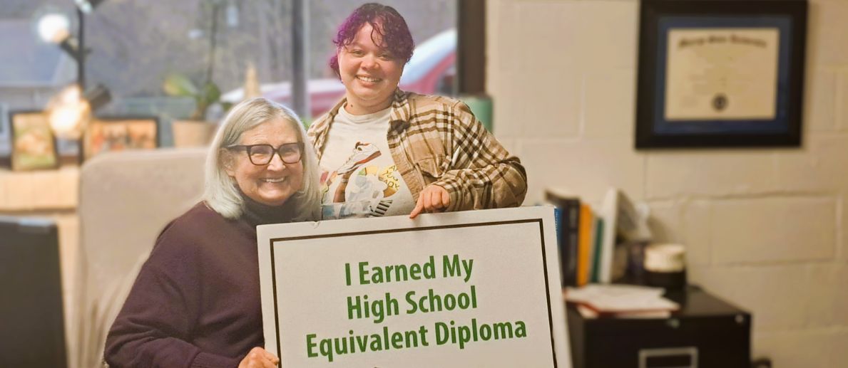 Adult Education Two women smile while holding sign that says I Earned My High School Equivalent Diploma